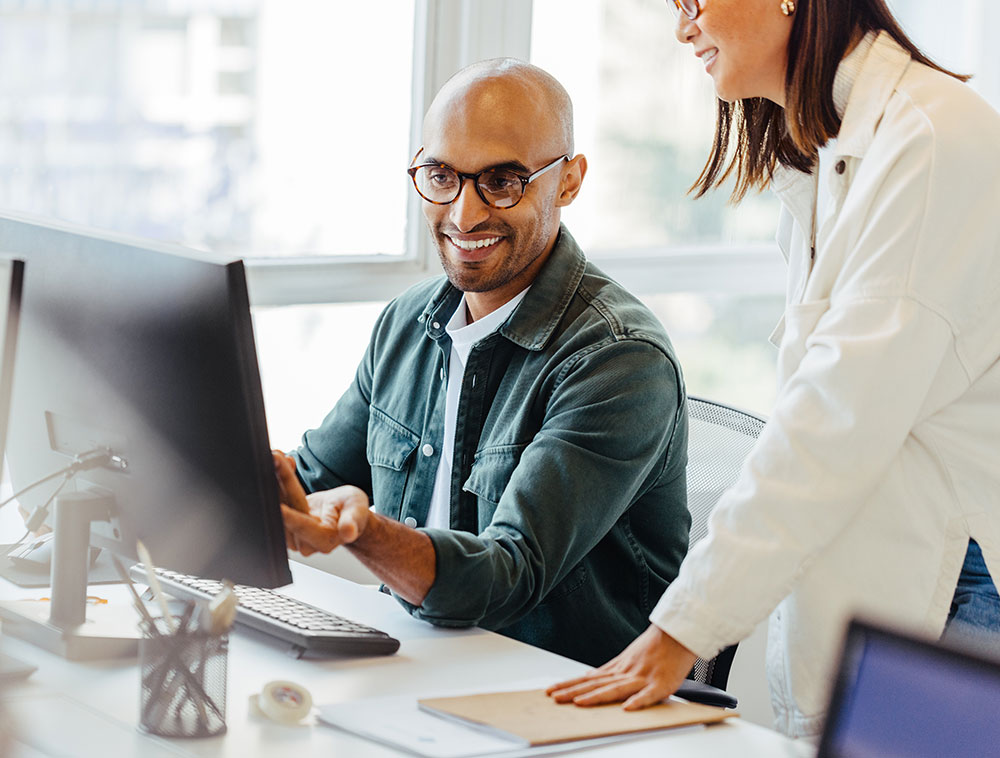 Man and woman smiling while looking at computer in office